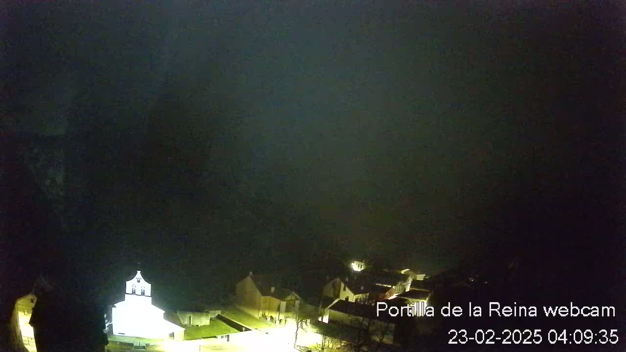 A nighttime, foggy view of a small village with a brightly lit church.