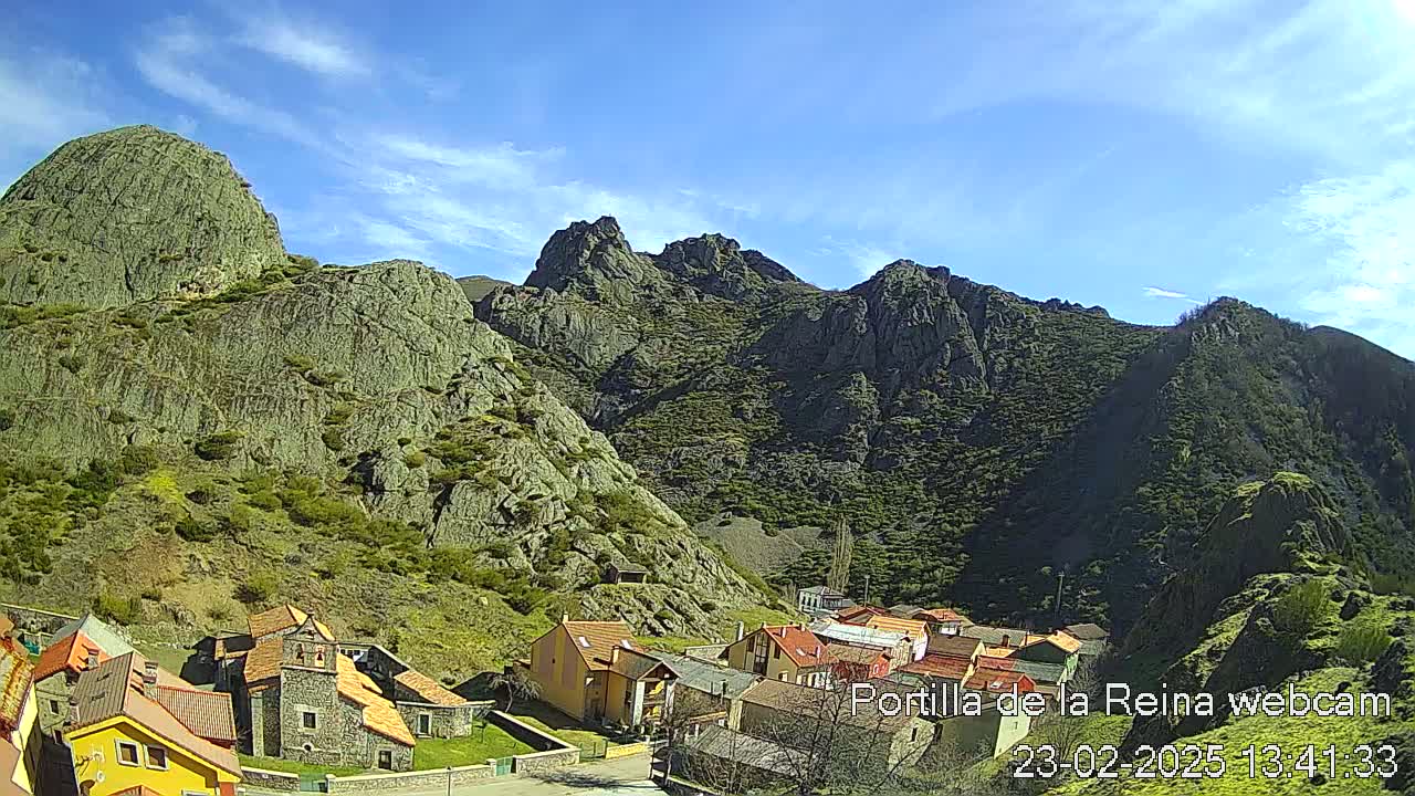 A small village nestled in a valley between rugged, rocky mountains under a mostly sunny sky.
