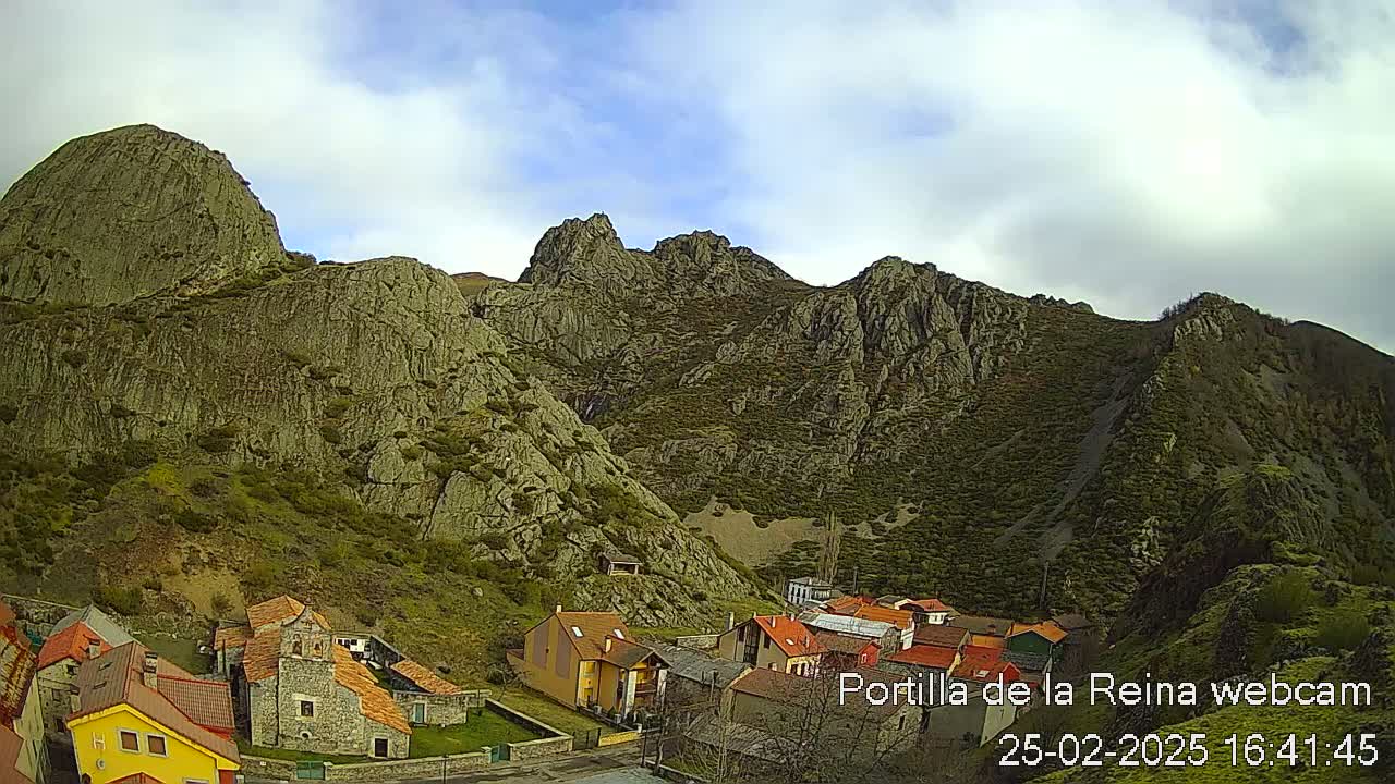 A small village nestled in a valley surrounded by rocky, mountainous terrain under a partly cloudy sky.