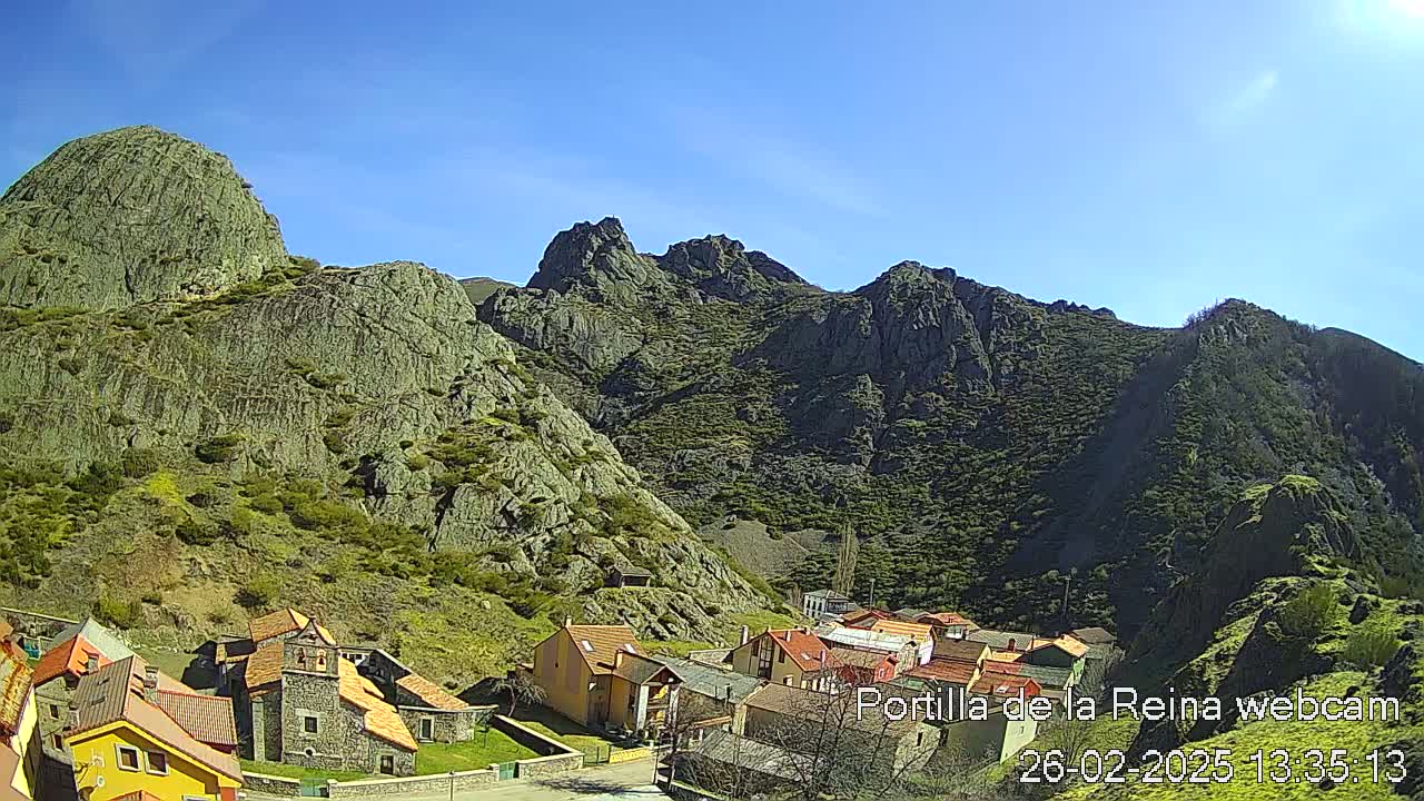 A small village nestled in a valley surrounded by steep, rocky mountains under a clear blue sky.