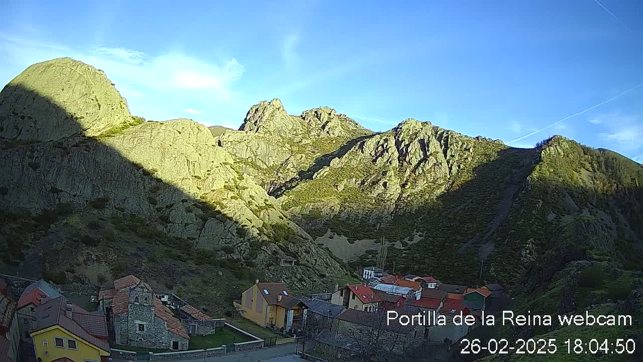 A small village nestled in a valley between sunlit, rocky mountains under a clear blue sky.
