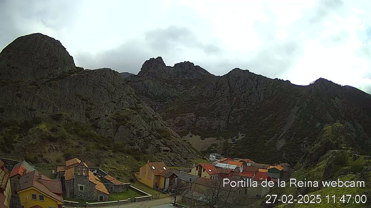 A small village nestled in a valley surrounded by dark, rocky mountains under an overcast sky.