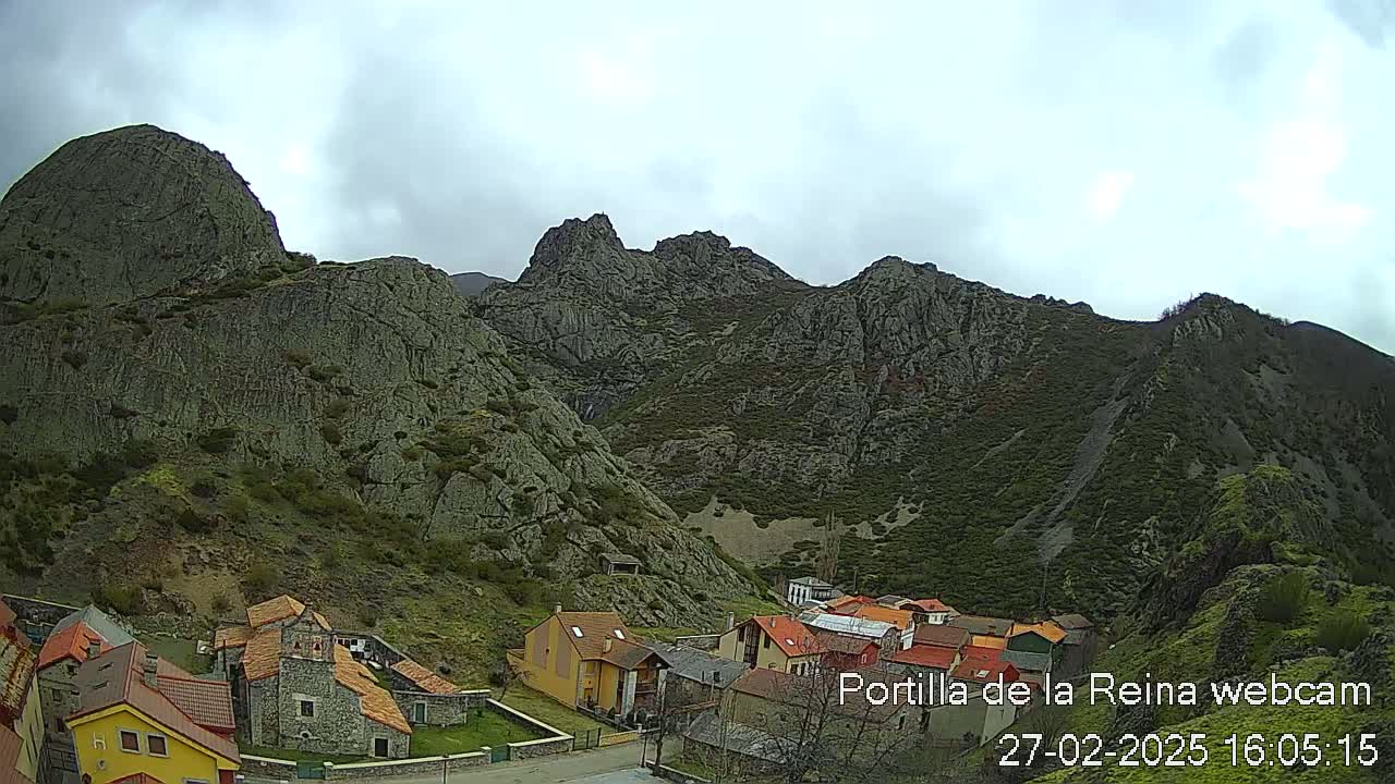 A small village nestled in a valley between rocky mountains under an overcast sky.