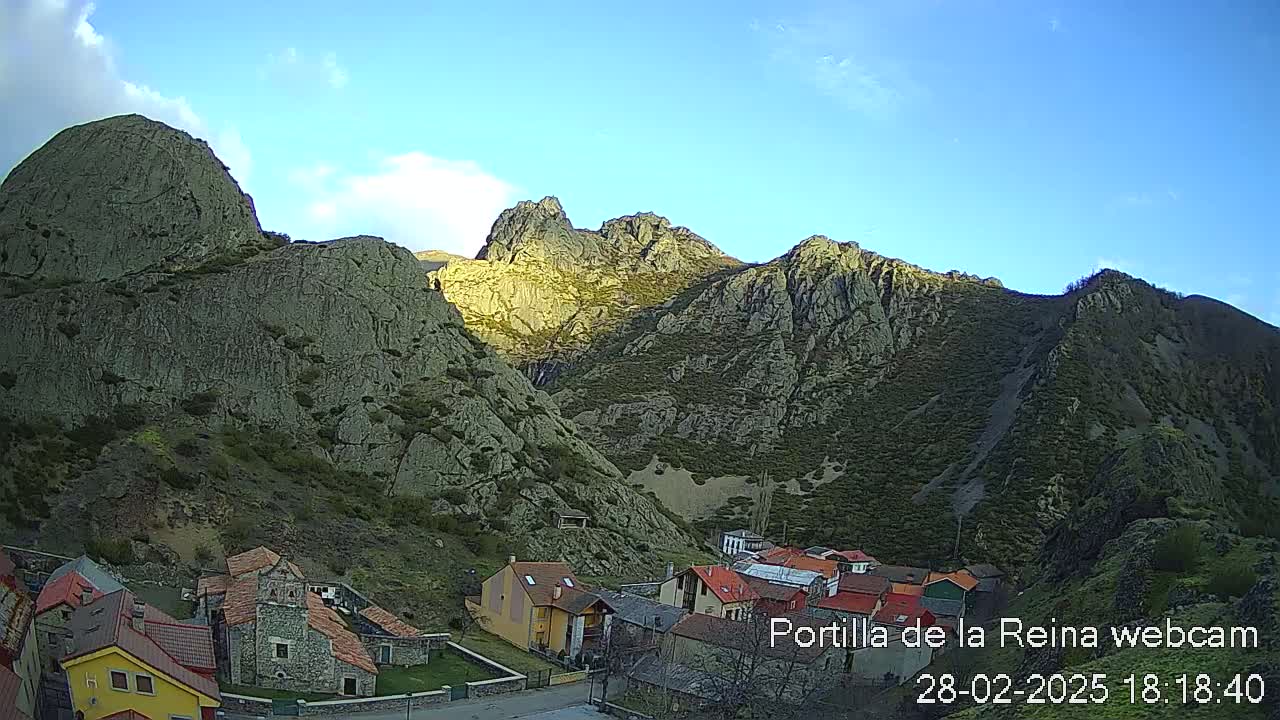 A small village nestled at the base of large, rocky mountains under a clear, mostly sunny sky.
