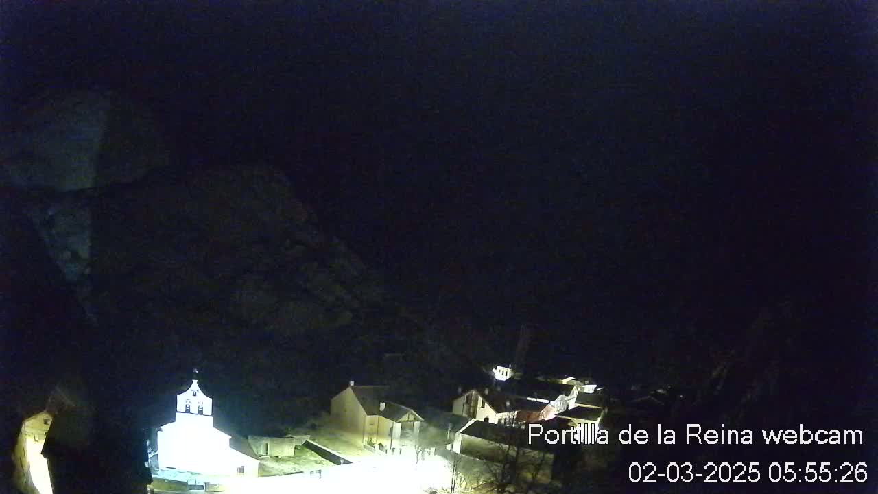 A nighttime, high-angle view shows a small village nestled in a dark, mountainous area, with some buildings faintly illuminated.
