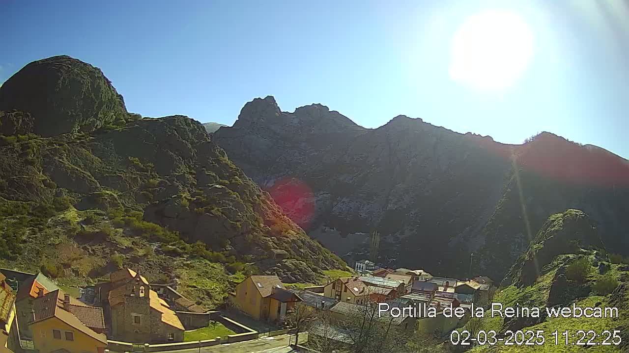 A small village nestled in a valley between rugged, dark mountains under a bright, sunny sky.