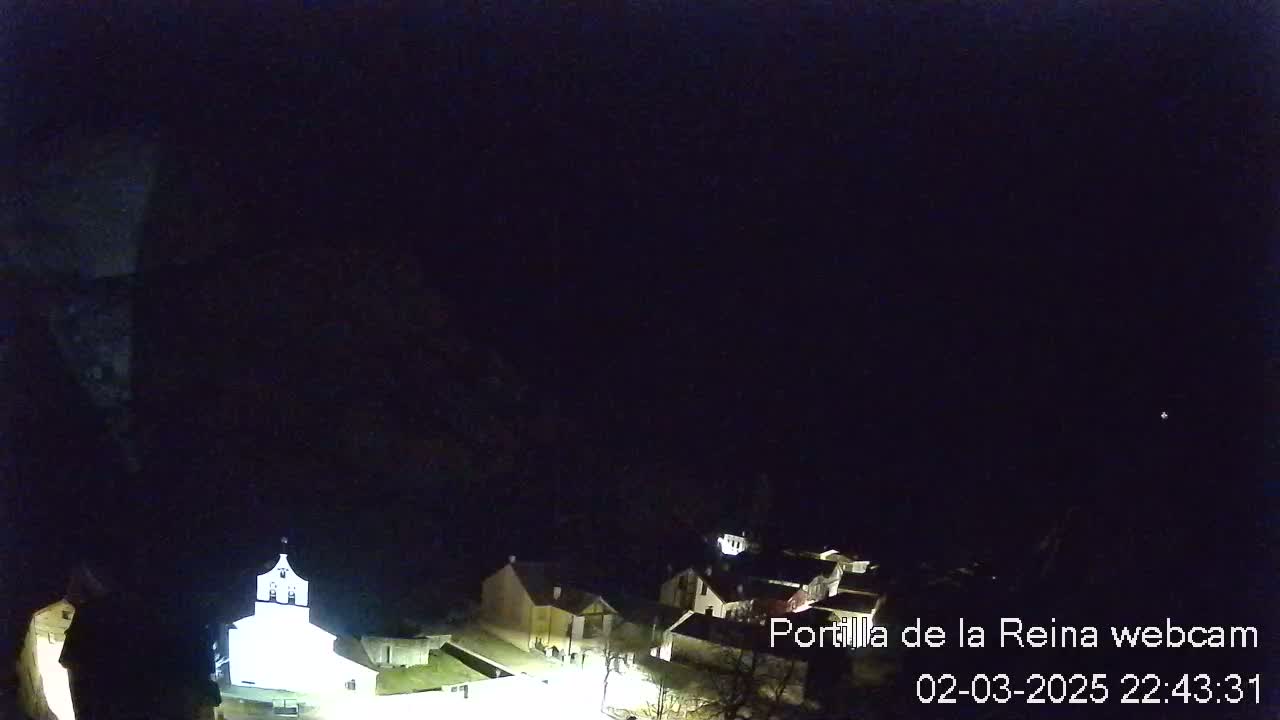 A nighttime, long shot of a small village illuminated with lights under a dark, clear sky.