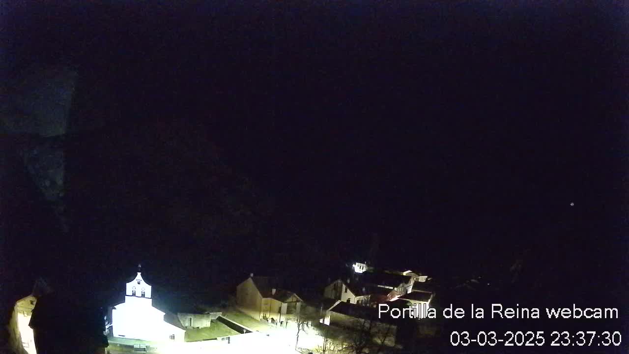 A nighttime long shot of a small village nestled in a dark landscape under a clear, starlit sky.