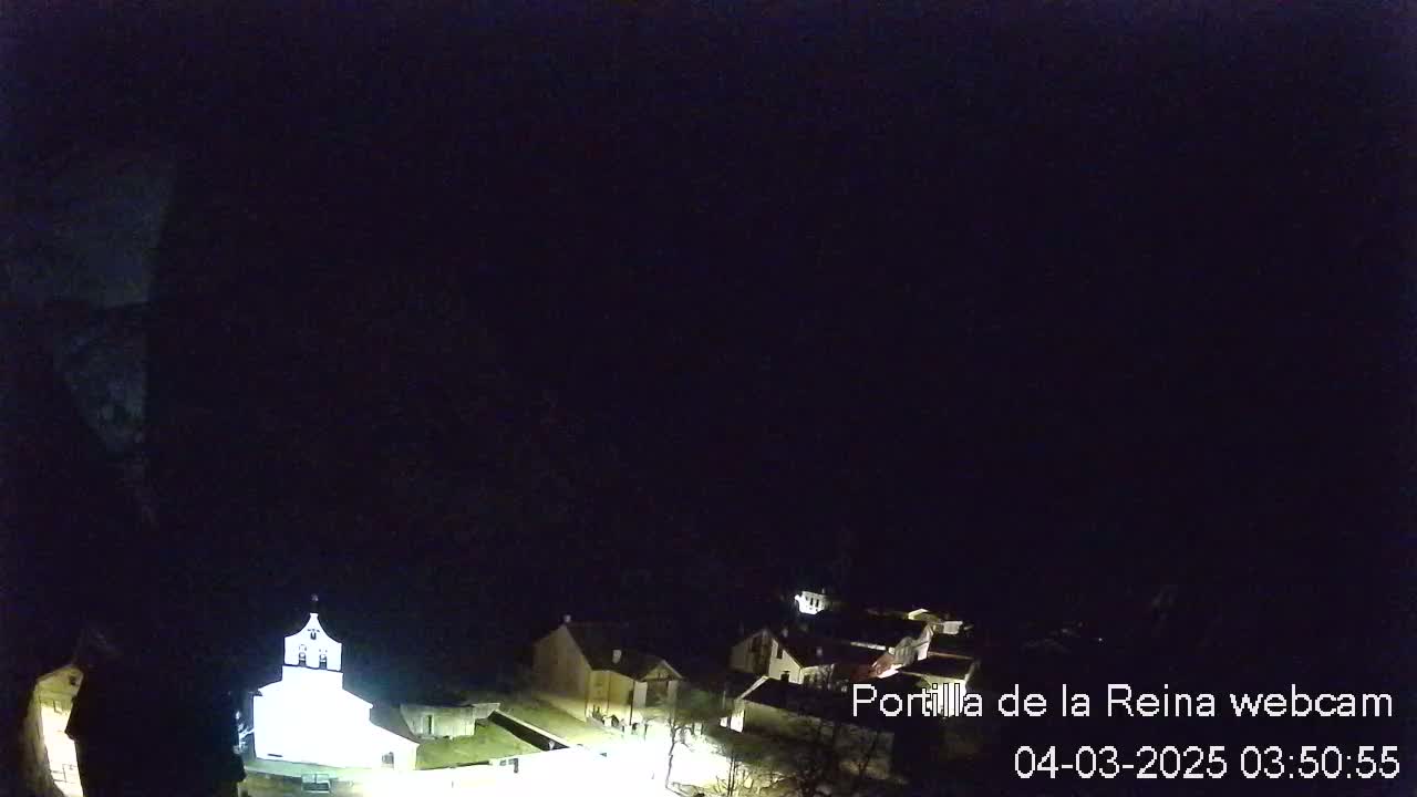A nighttime view of a small village with a brightly lit church, under a dark, clear sky.