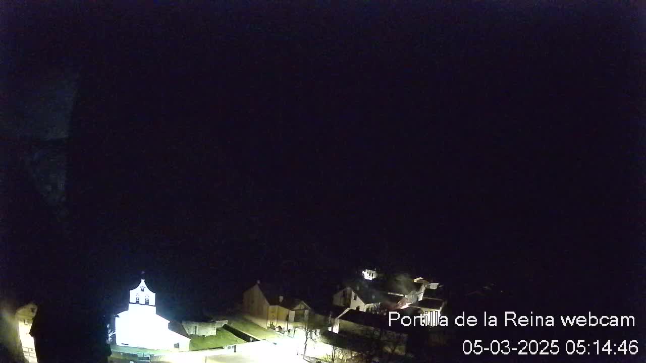 A nighttime, high-angle view shows a small village with a brightly lit church, under a dark, clear sky.