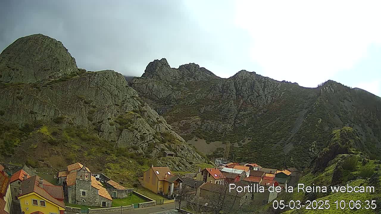 A small village nestled in a valley surrounded by imposing, rocky mountains under an overcast sky.