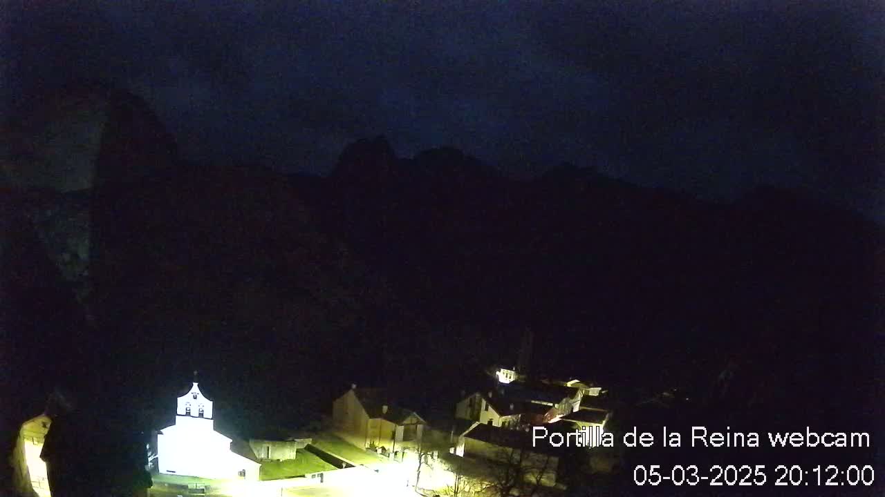 A small, illuminated village nestled at the base of dark mountains under a night sky.