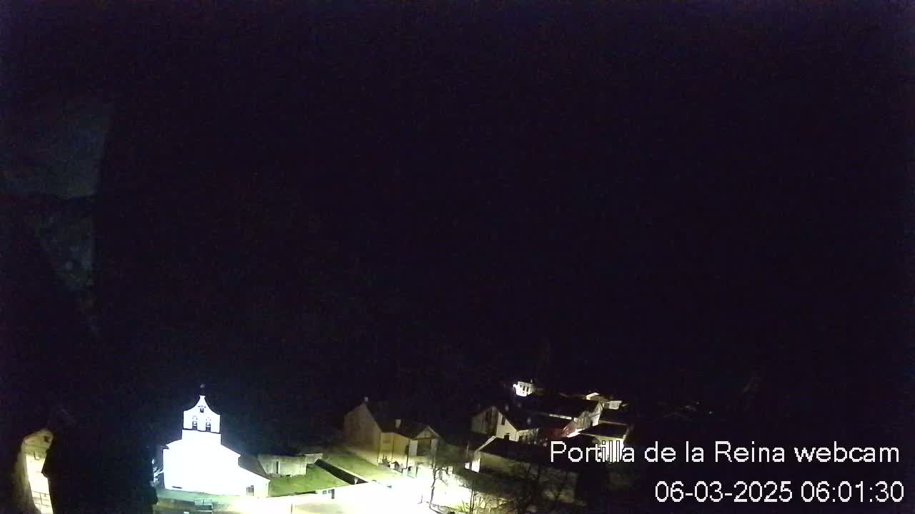 A small, dimly lit village is visible at night under a dark sky.