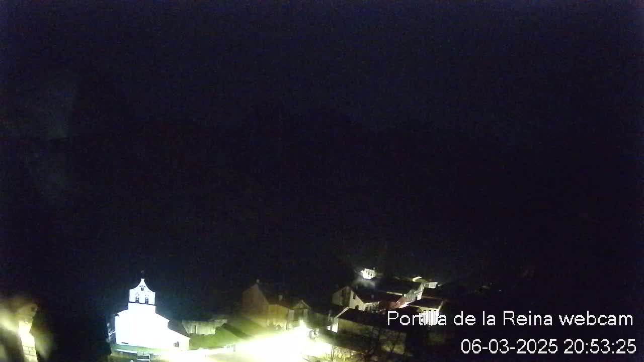 A small village at night is illuminated, with a church prominently lit in the center, under a dark, clear sky.