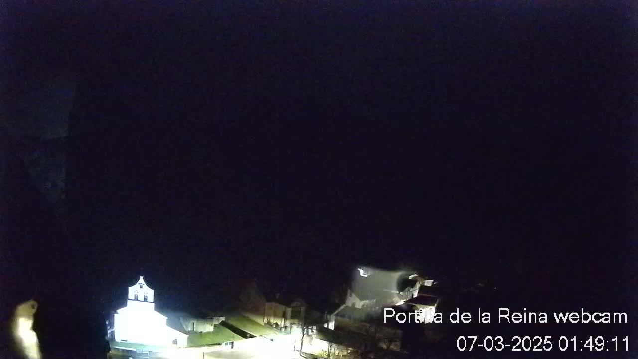 A nighttime view of dimly lit buildings and a tall, light-colored structure under a dark, clear sky.