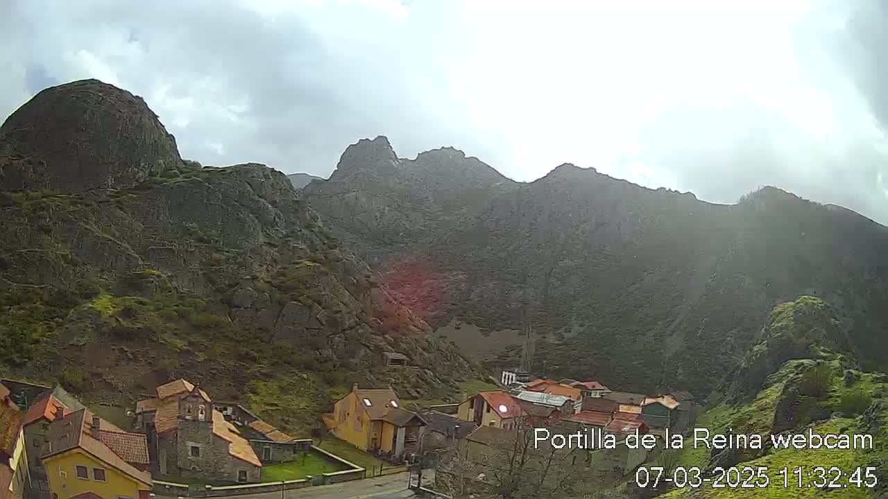 A small village nestled in a valley surrounded by rocky mountains under an overcast sky.