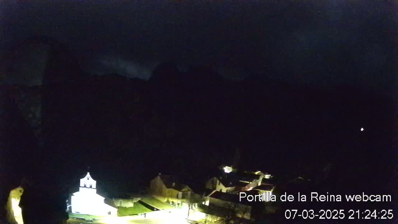 A nighttime view of a small village nestled in a dark valley, under a mostly clear, dark sky.