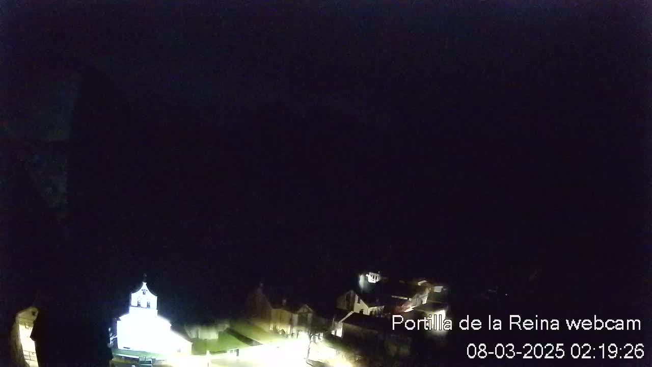 A nighttime, high-angle view shows a small town with dimly lit buildings under a dark, clear sky.