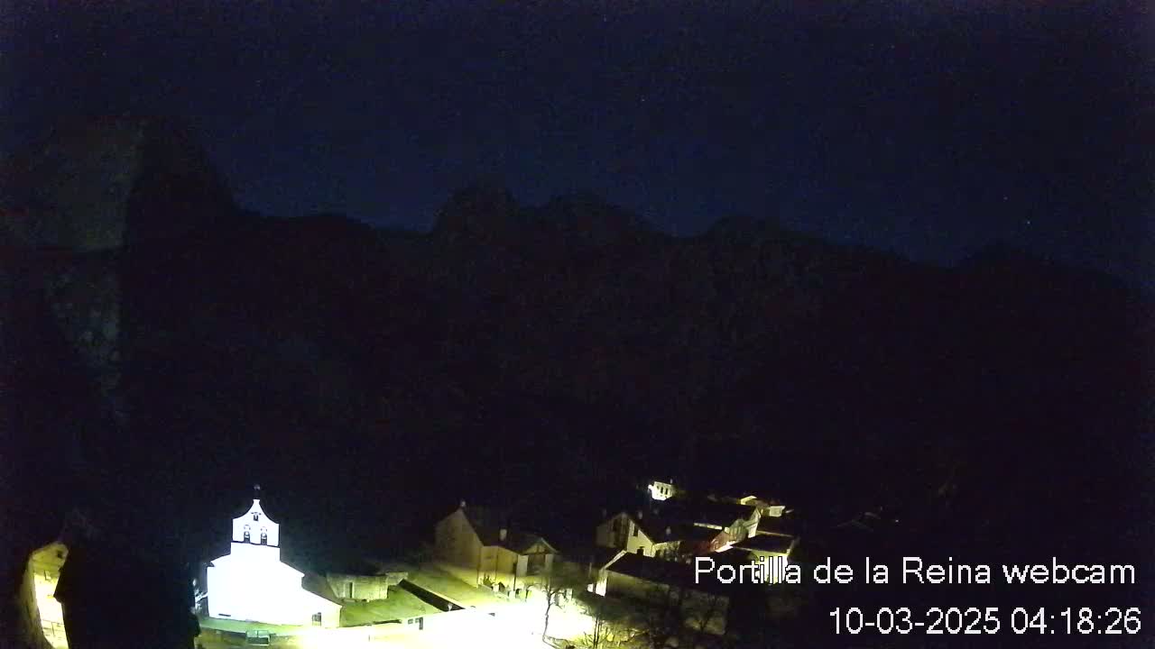 A small, dimly lit village nestled at the base of dark mountains under a night sky.