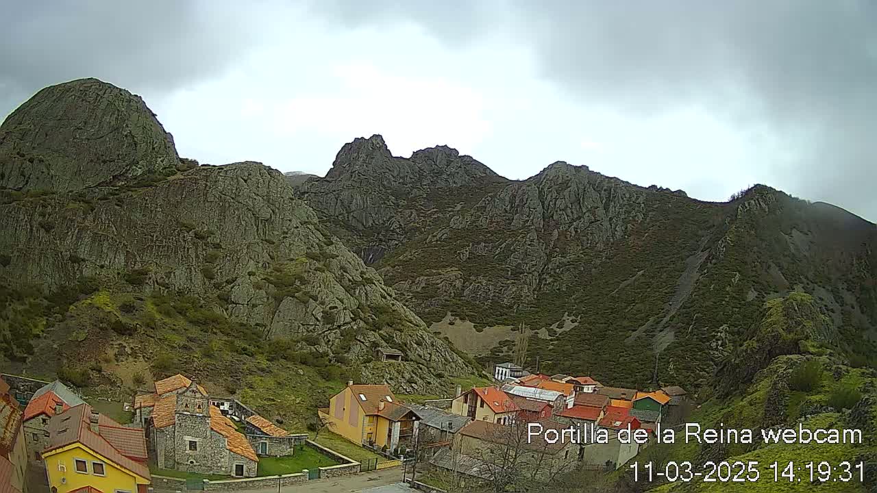 A small village nestled in a valley surrounded by steep, rocky mountains under an overcast sky.