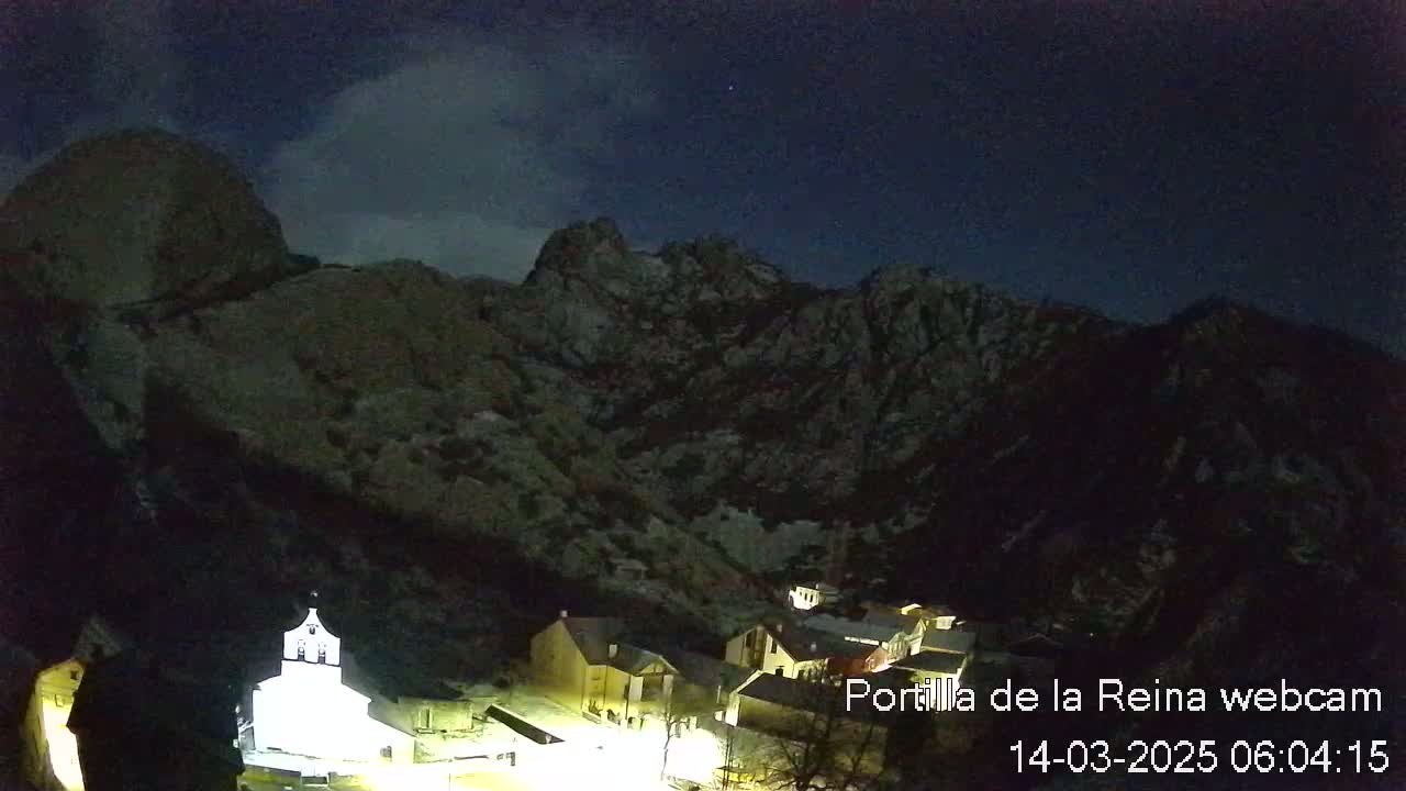 A small village nestled in a valley between dark, rocky mountains under a partly cloudy night sky.