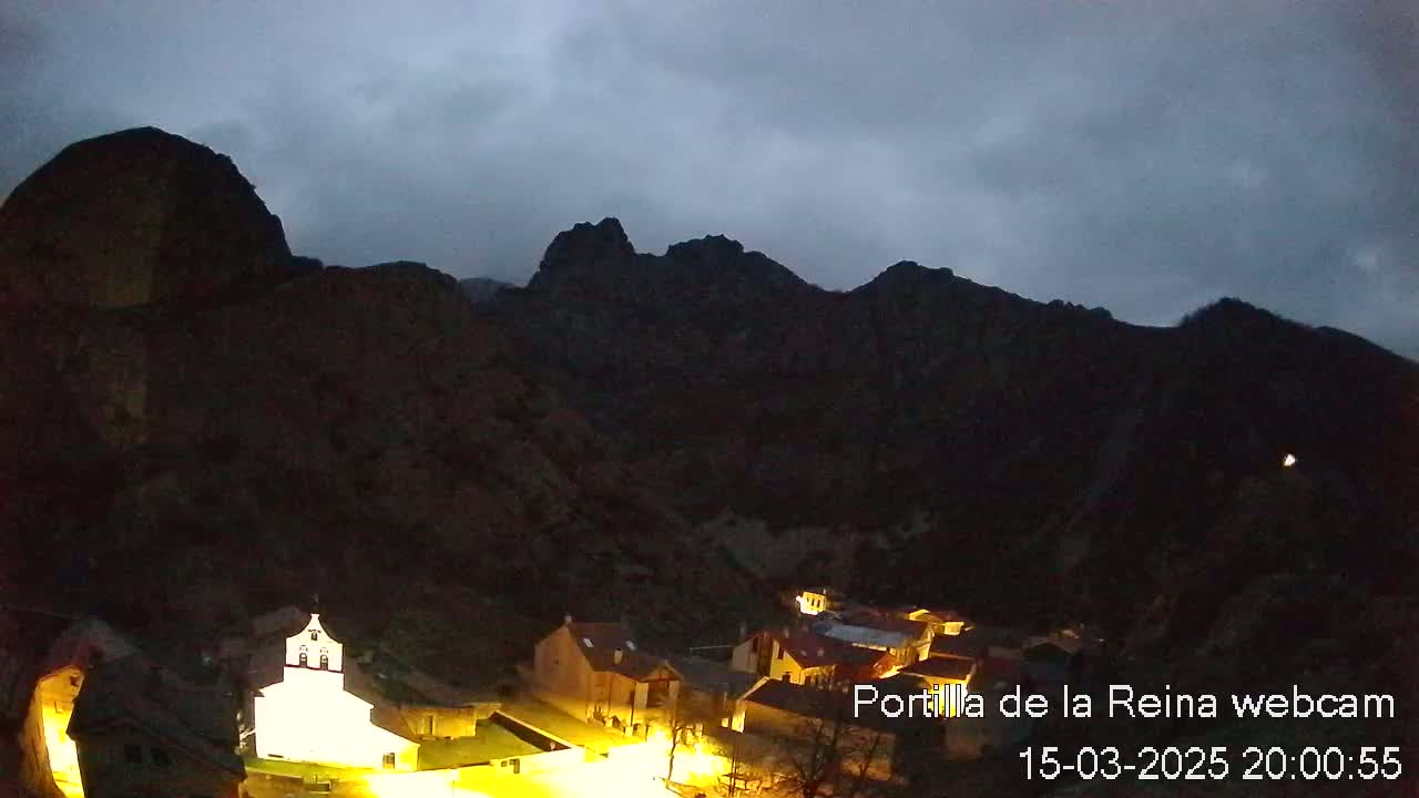 A small, illuminated village nestled in a dark, mountainous valley under an overcast sky.