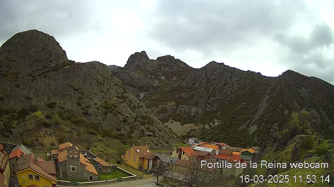 A small village nestled in a valley surrounded by rugged, grey mountains under an overcast sky.