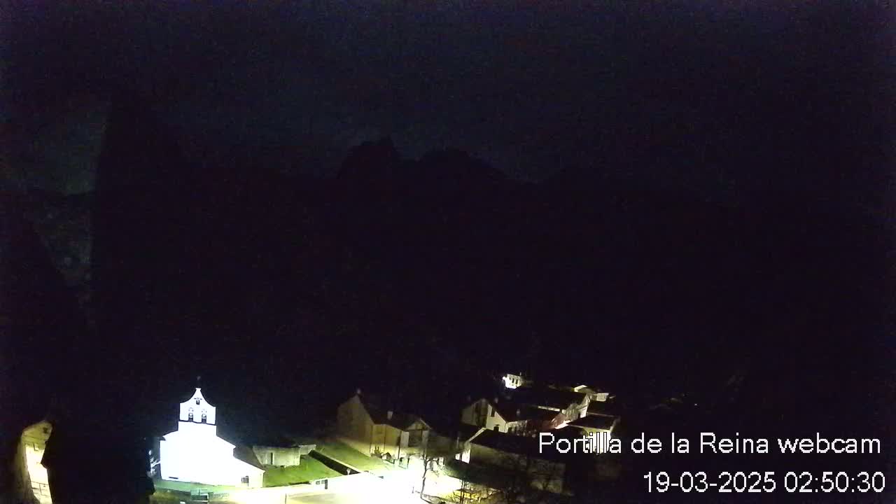 A nighttime, dimly lit village nestled beneath dark mountains.