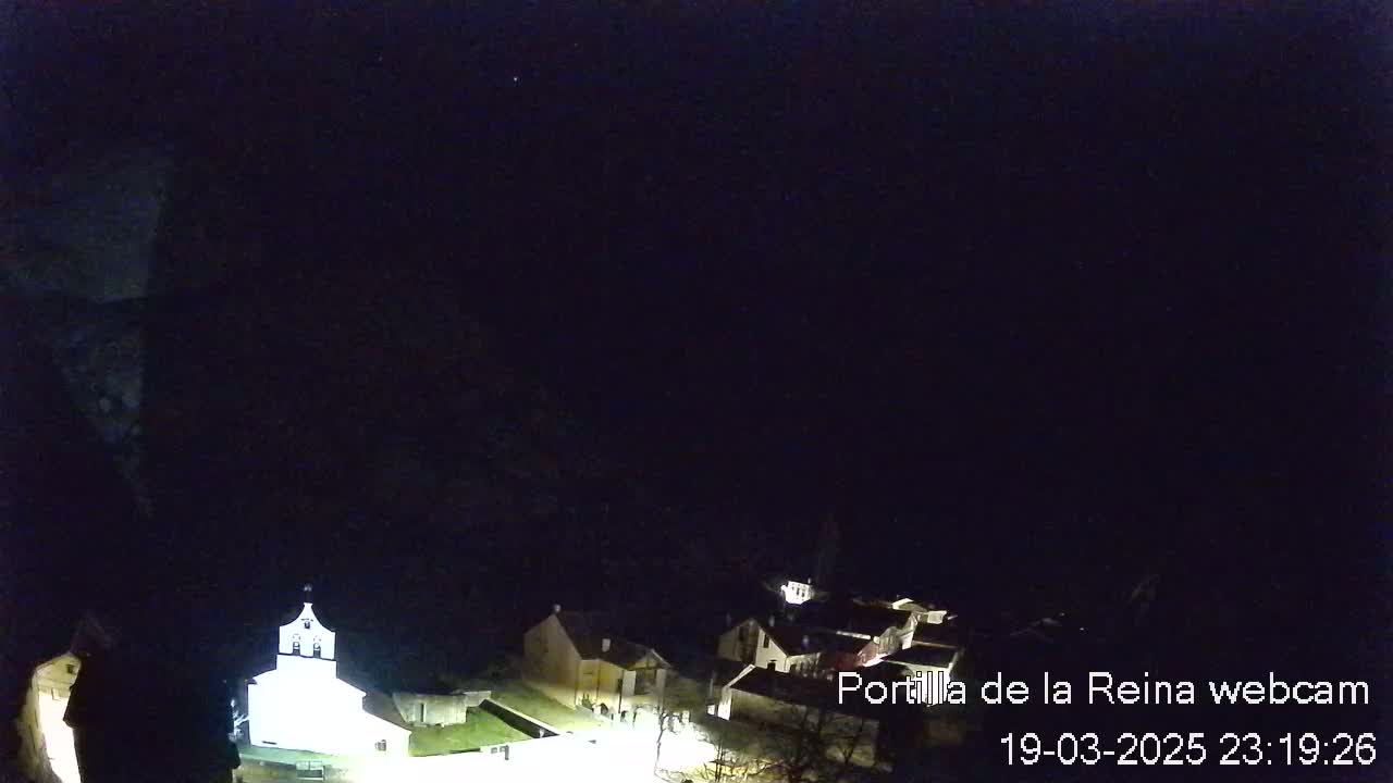 A nighttime, aerial view shows a small village nestled in a dark, mountainous landscape.