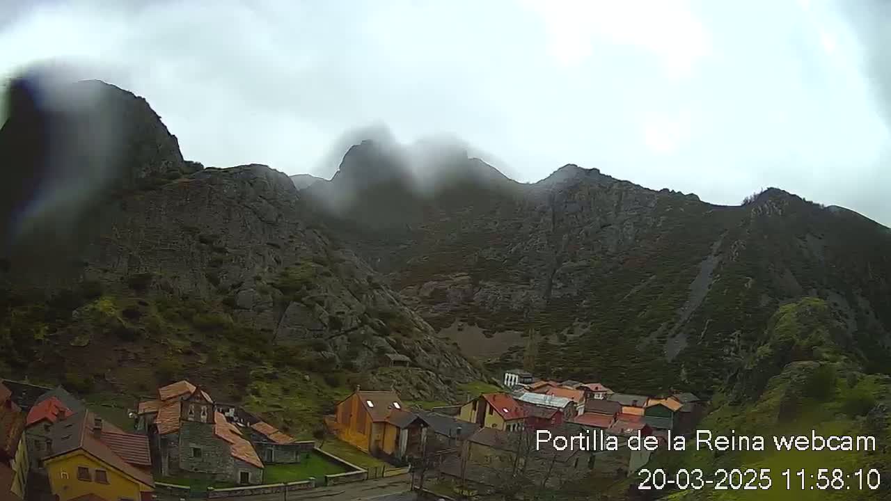 A small village nestled in a valley surrounded by rocky mountains under a cloudy sky.