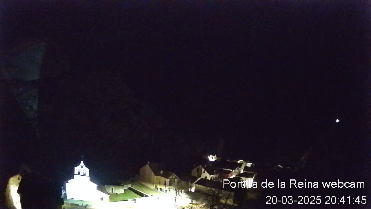 A nighttime, aerial view shows a small village with a brightly lit church under a clear, dark sky.