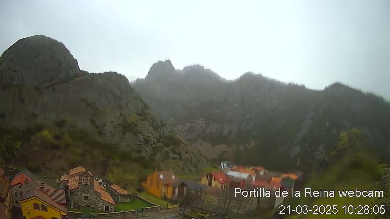 A misty mountain range overlooks a small village of stone and brightly colored houses.