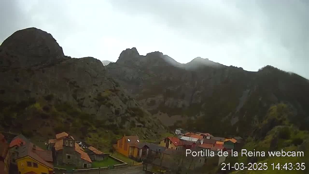 A small village nestled in a valley surrounded by rocky mountains under an overcast sky.