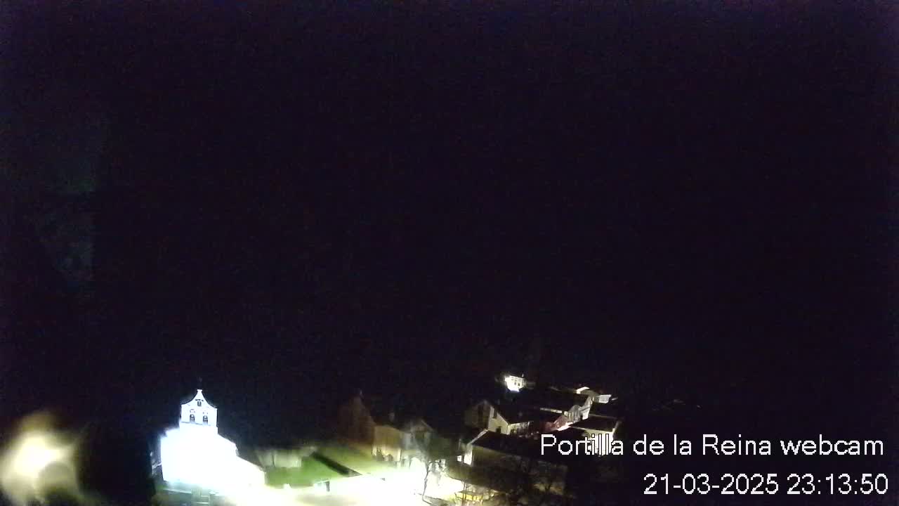 A nighttime, high-angle view shows a dimly lit village with a brightly lit building that appears to be a church.