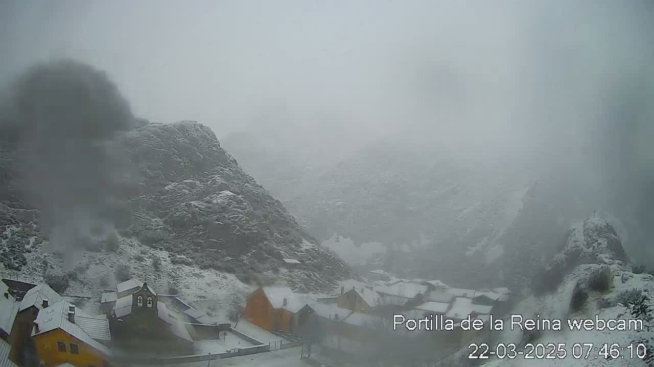 A snow-covered village nestled in a mountainous valley is shrouded in heavy fog.