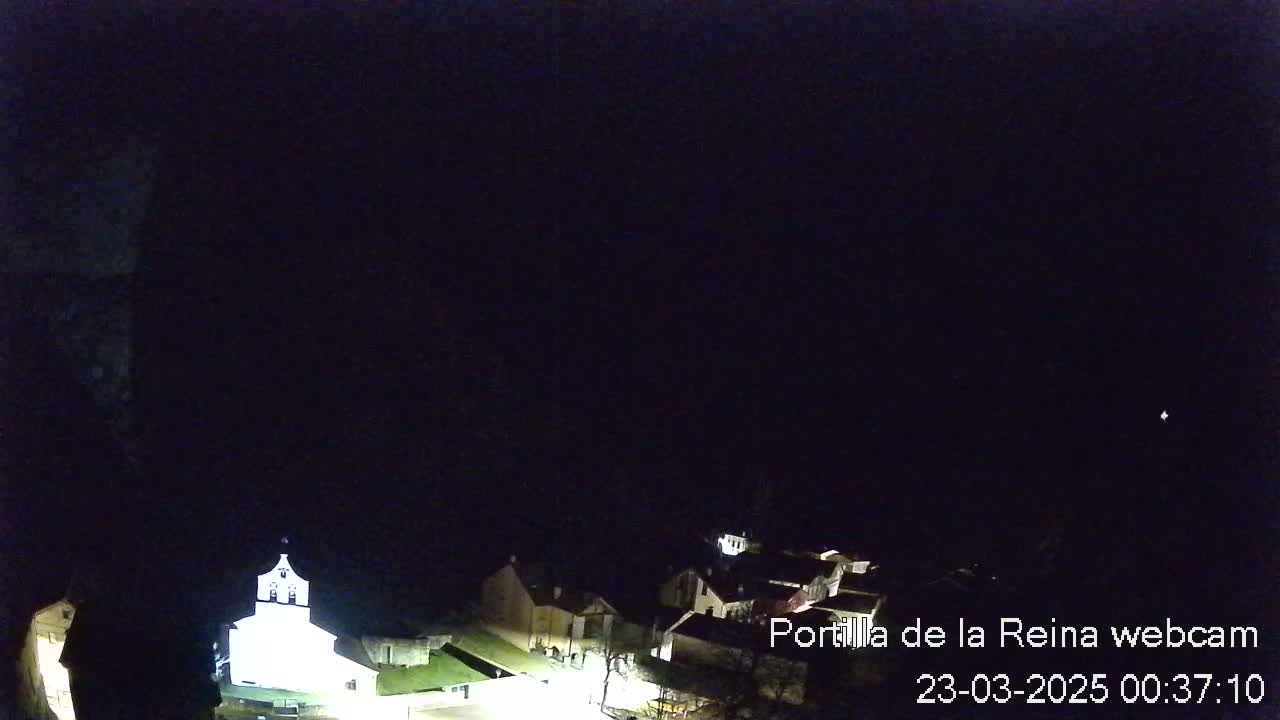 A nighttime, high-angle view shows a dimly lit village with a church, under a dark, clear sky.