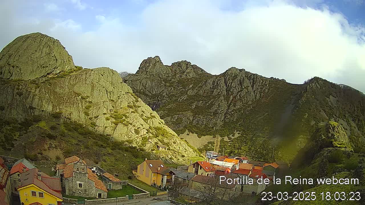A small village nestled in a valley between steep, rocky mountains under a partly cloudy sky.