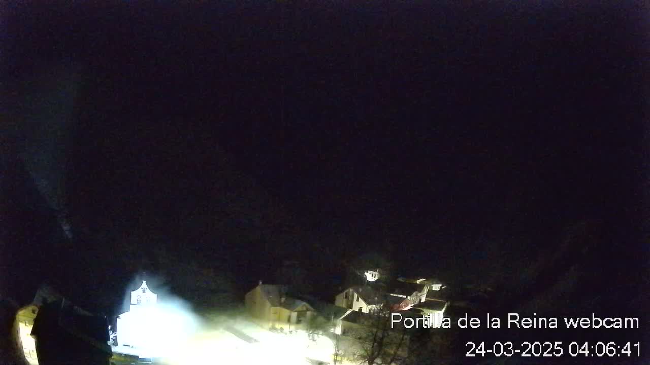 A nighttime, dimly lit view of a small village, possibly with snow on the ground, under a dark sky.
