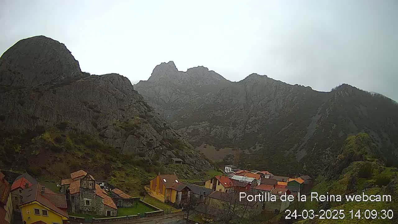 A small village nestled in a valley between steep, rocky mountains under an overcast sky.