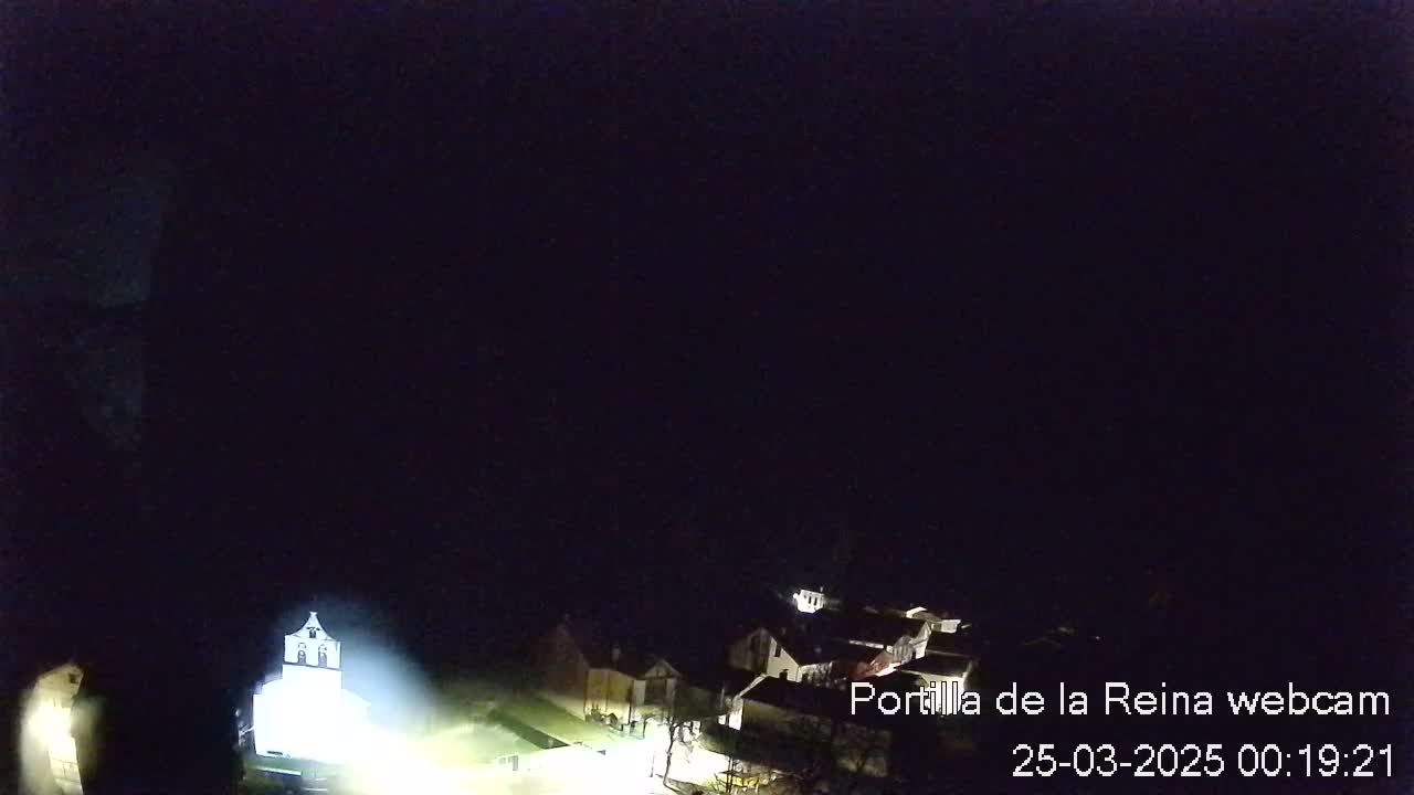 A nighttime, overhead view of a small village with a brightly lit church.