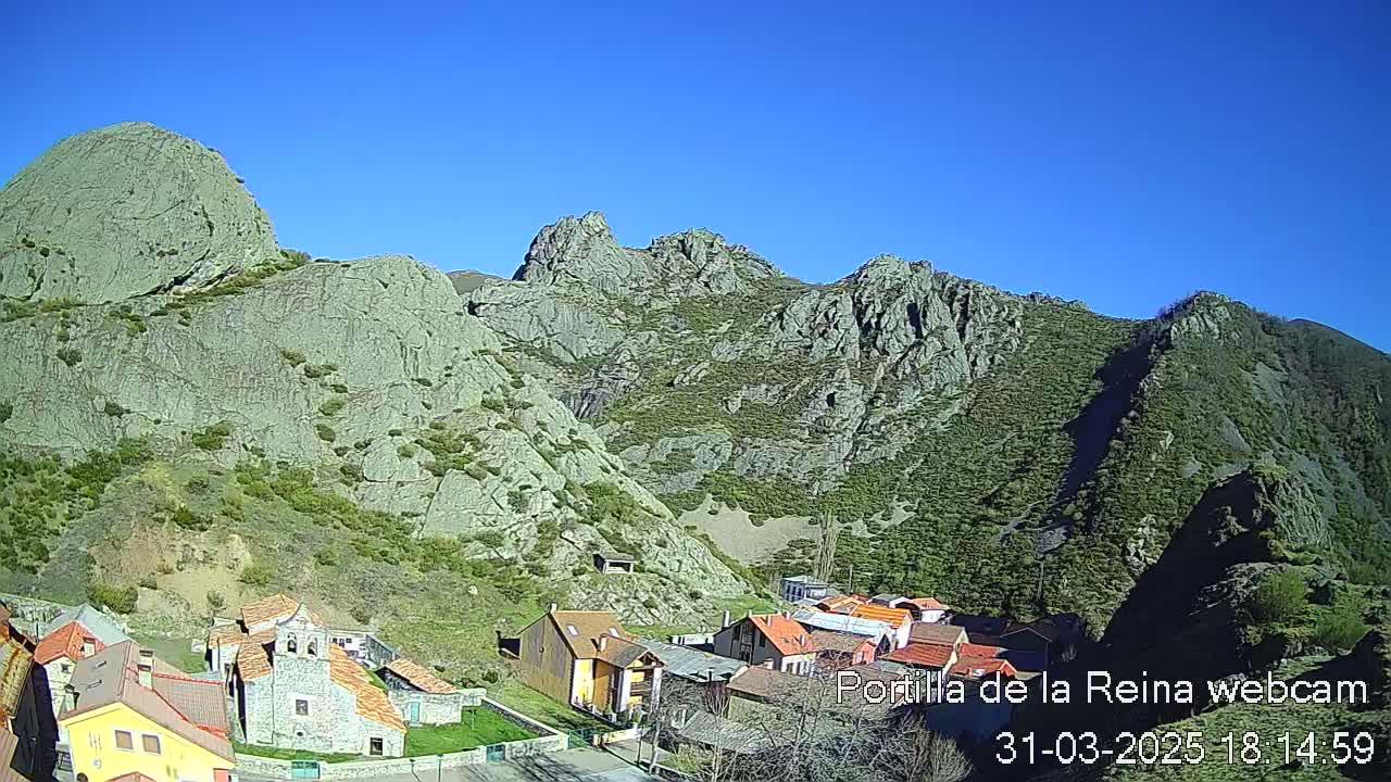 A small village nestled at the base of large, rocky mountains under a clear blue sky.