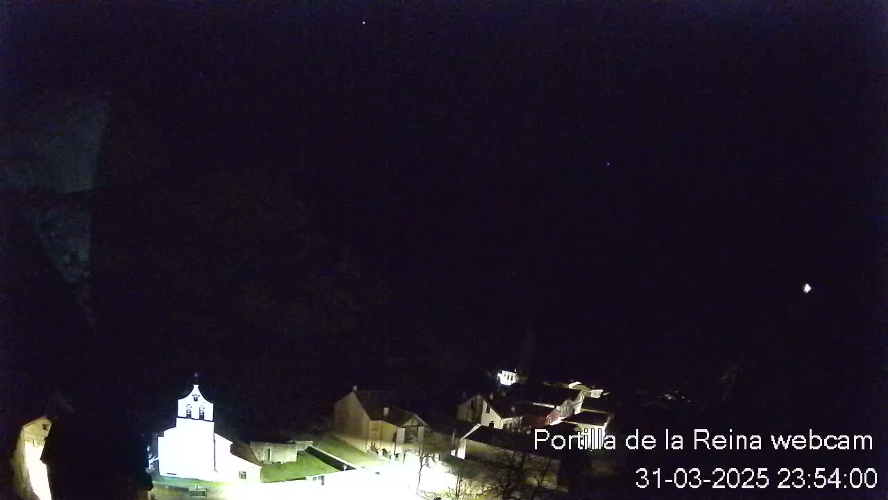 A nighttime, long shot of a small village nestled in a dark valley under a clear, starry sky.