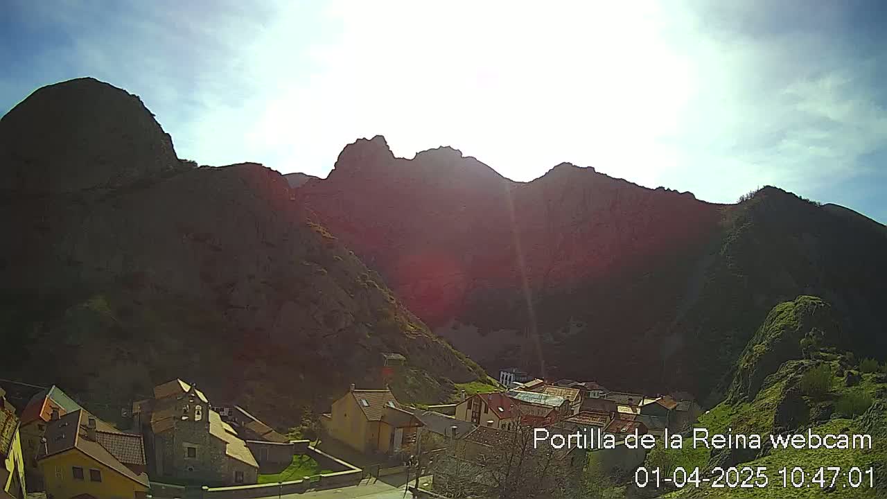 A small village nestled in a valley between sunlit, dark-colored mountains under a mostly clear sky.