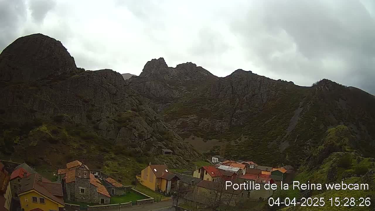 A small village nestled at the base of a rocky mountain range under an overcast sky.