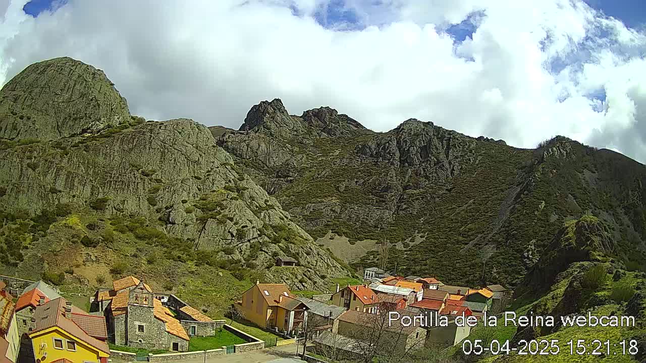 A small village nestled in a valley between rocky, green mountains under a partly cloudy sky.