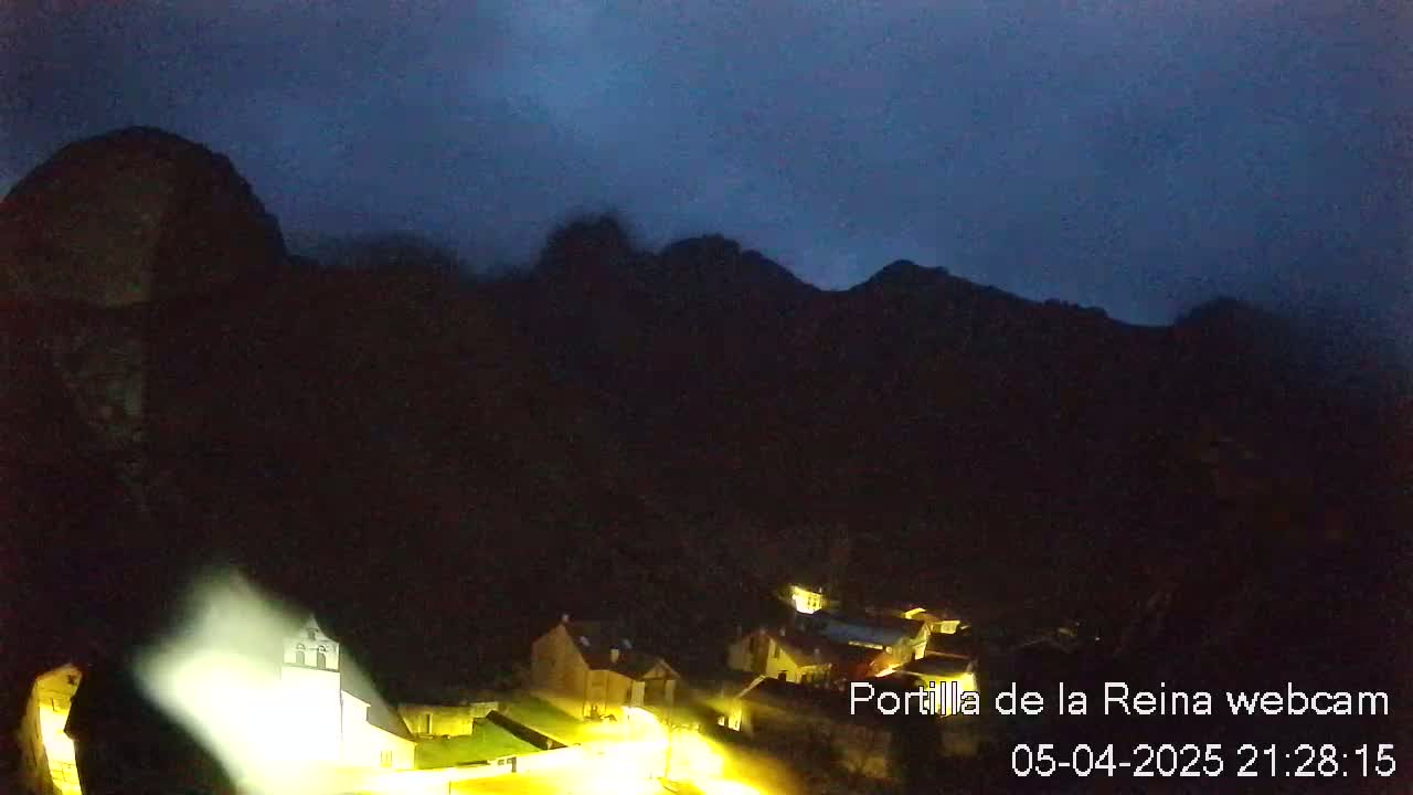 A small, dark village nestled in a valley between silhouetted mountains under a dark, possibly cloudy, night sky.