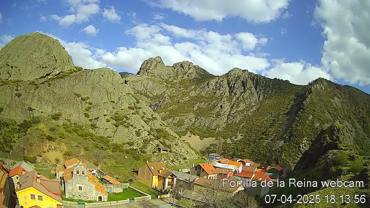 A small village nestled in a valley between rugged, rocky mountains under a partly cloudy sky.