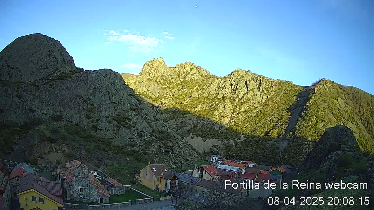 A small village nestled in a valley between large, rocky mountains under a clear blue sky.
