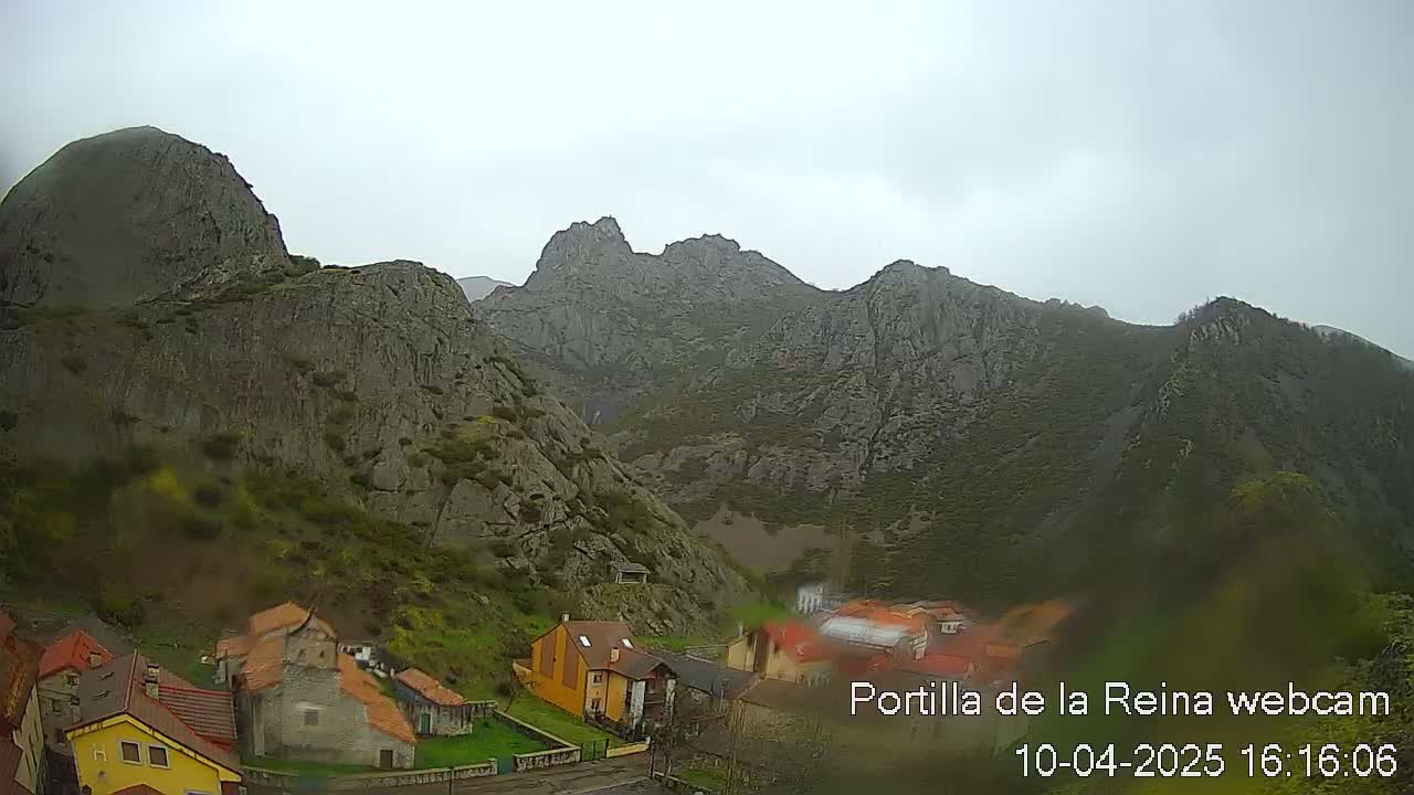 A small village nestled in a valley between large, gray, rocky mountains on an overcast day.