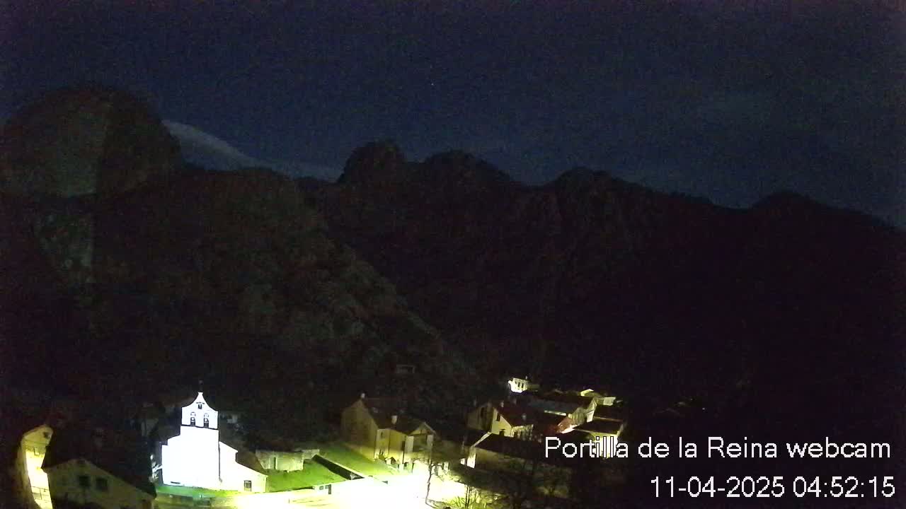 A small village nestled in a dark valley at night, illuminated by lights, is surrounded by mountains under a clear, dark sky.